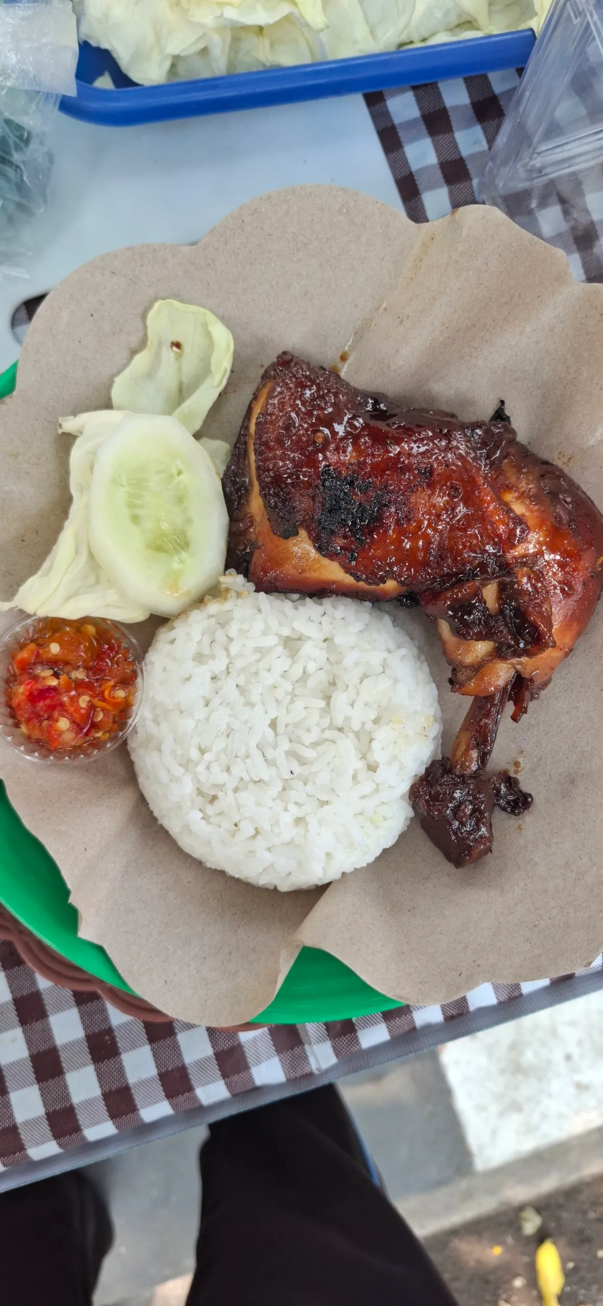 Ayam bakar kecap dengan nasi, sambal, timun, dan kol di atas kertas nasi.