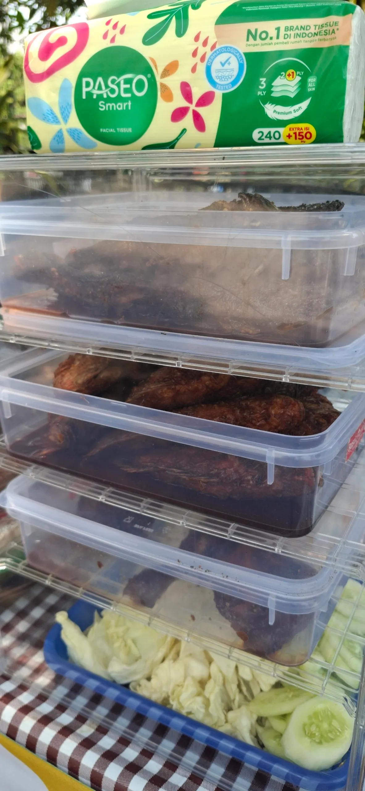 Etalase plastik bersusun berisi lauk bakar yang sudah matang, dengan kol dan timun di rak bawah.