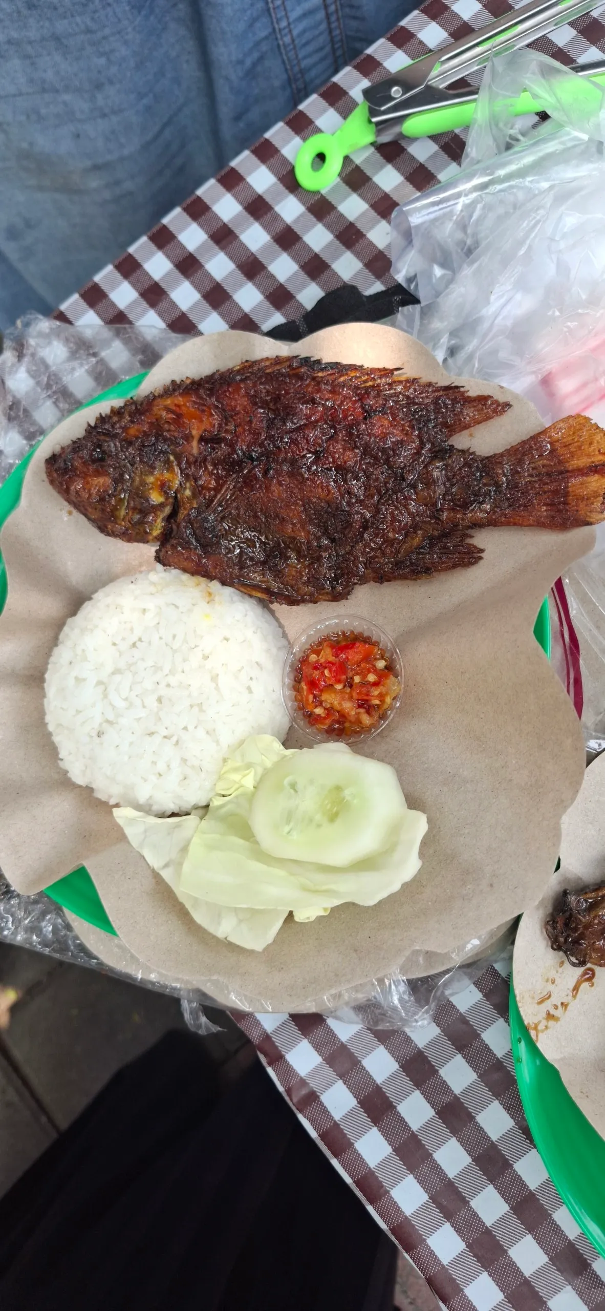 Kakap bakar utuh dengan nasi, sambal, timun, dan kol di atas kertas nasi.