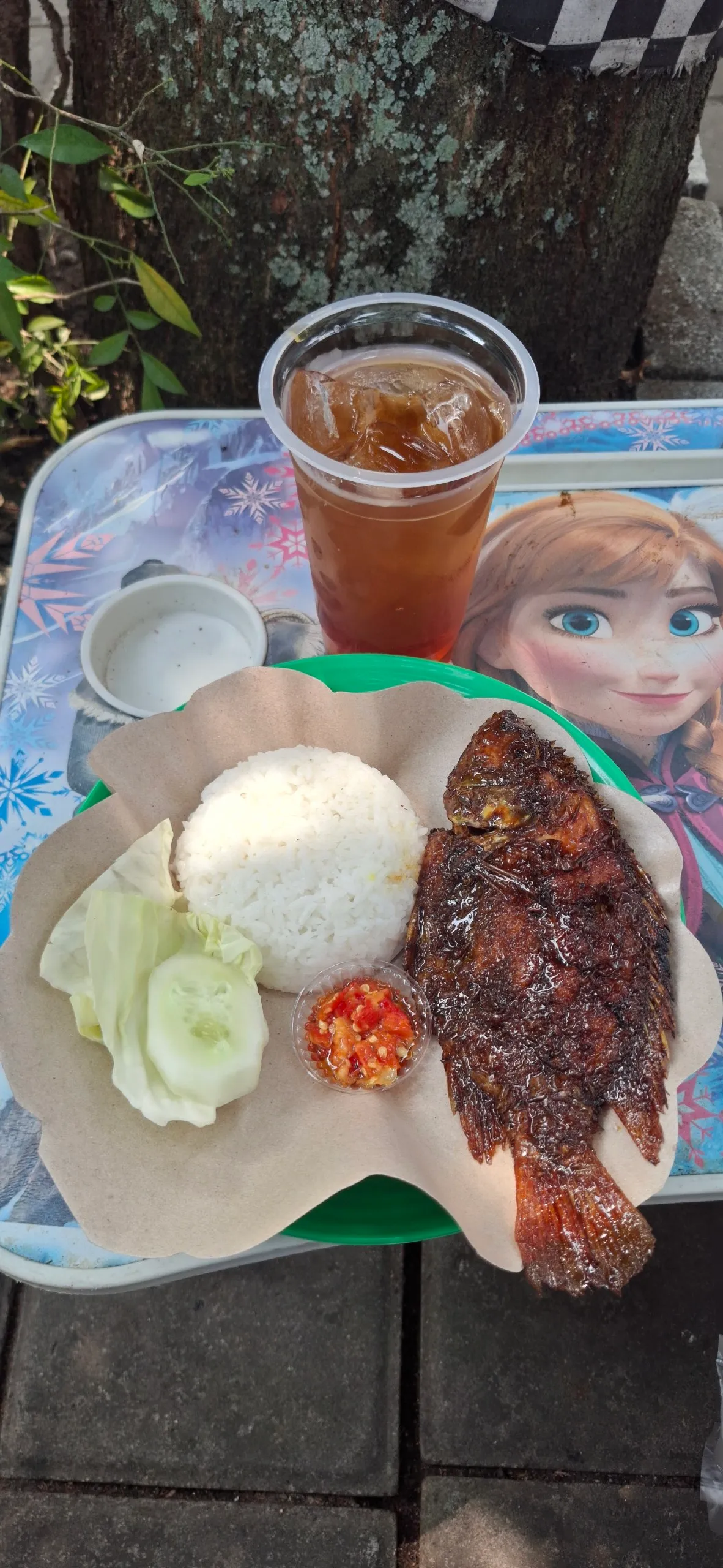 Sepiring kakap bakar, nasi, sambal, dan lalapan dengan segelas es teh di atas nampan.